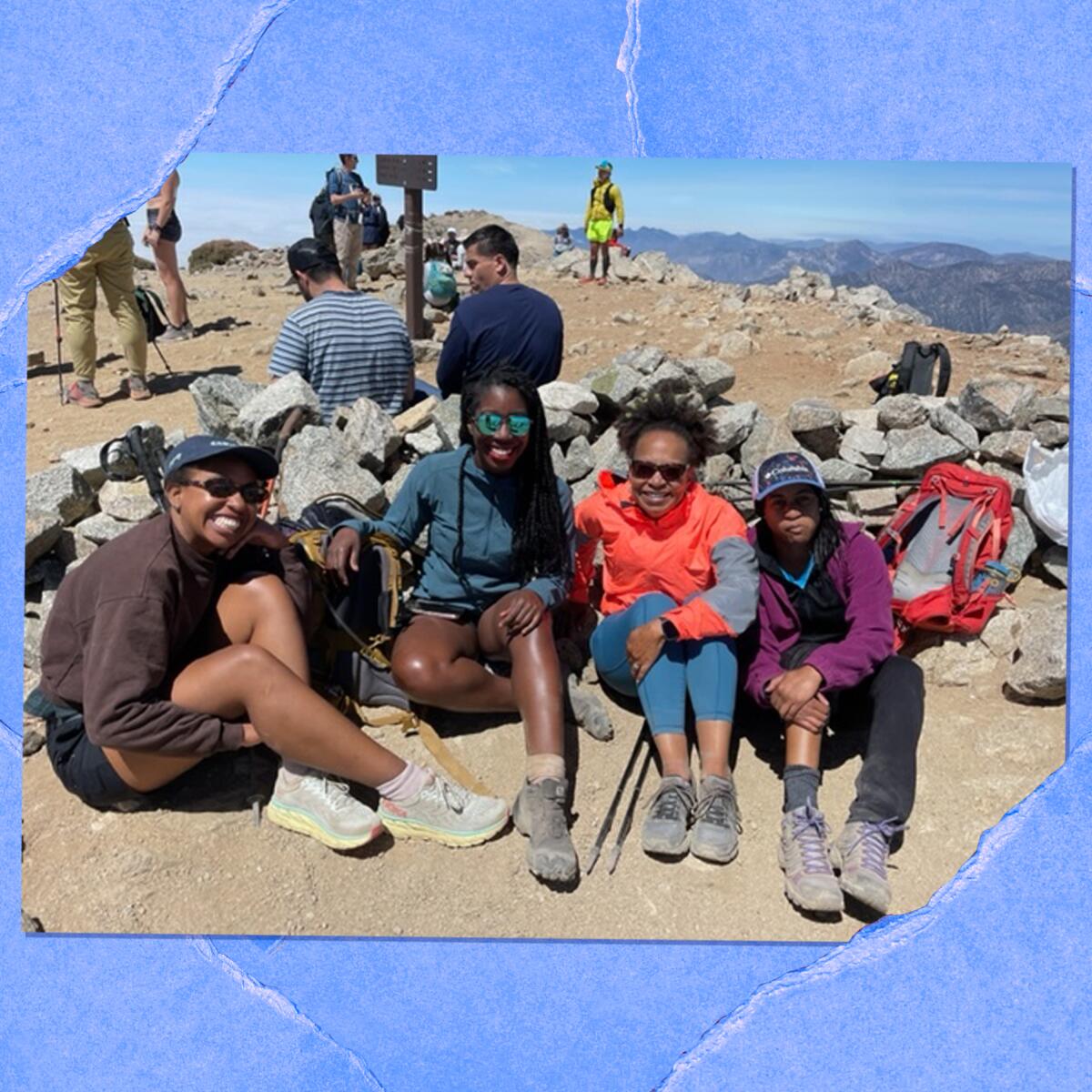 Photo of people sitting by a rock wall on top of a mountain.