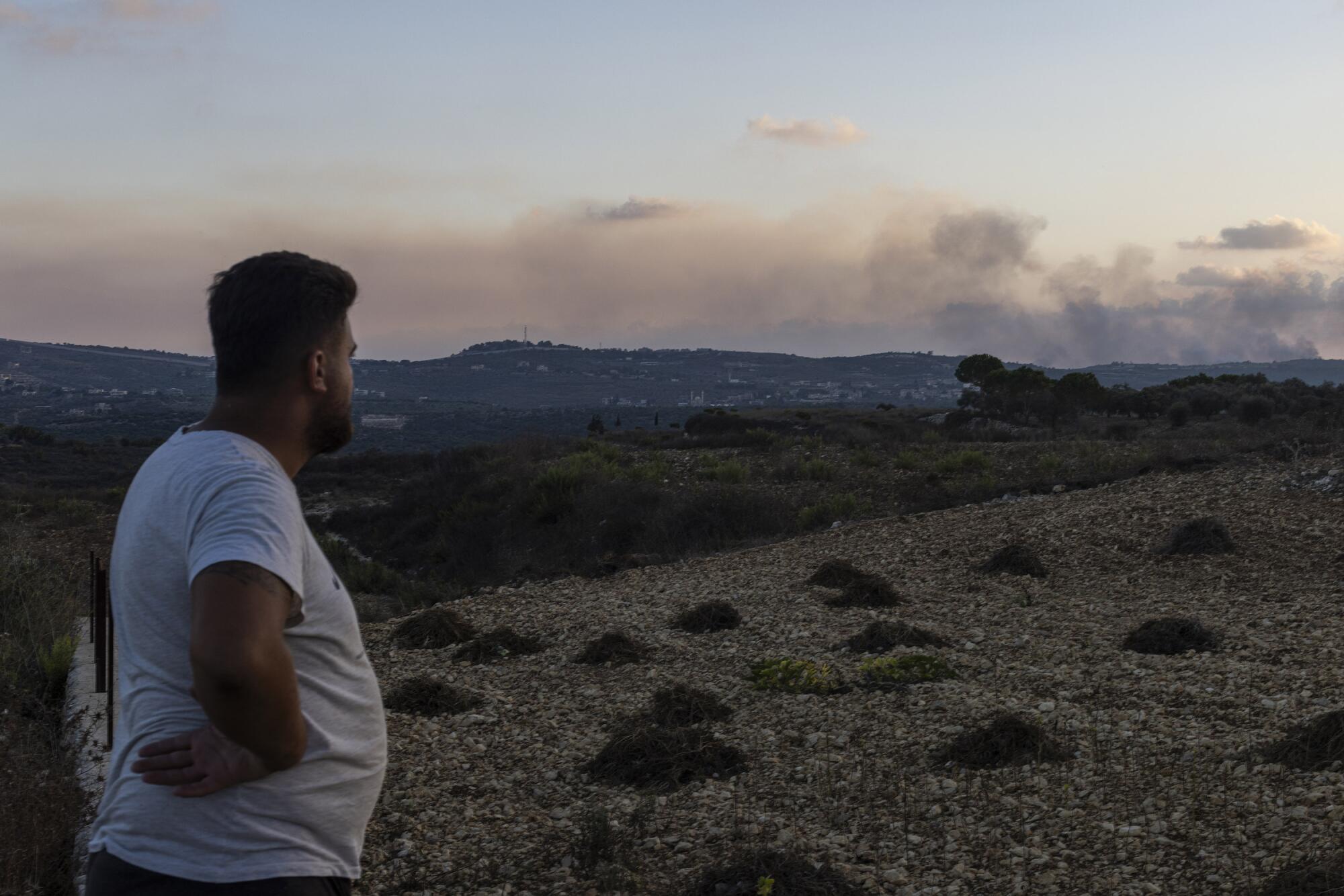 A man watches smoke rise over the distant hills.