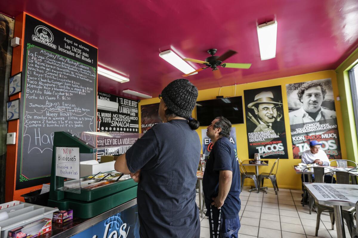 Customers checking out the menu at Tacos Los Desvelados, a drug lord-themed taqueria in Maywood.
