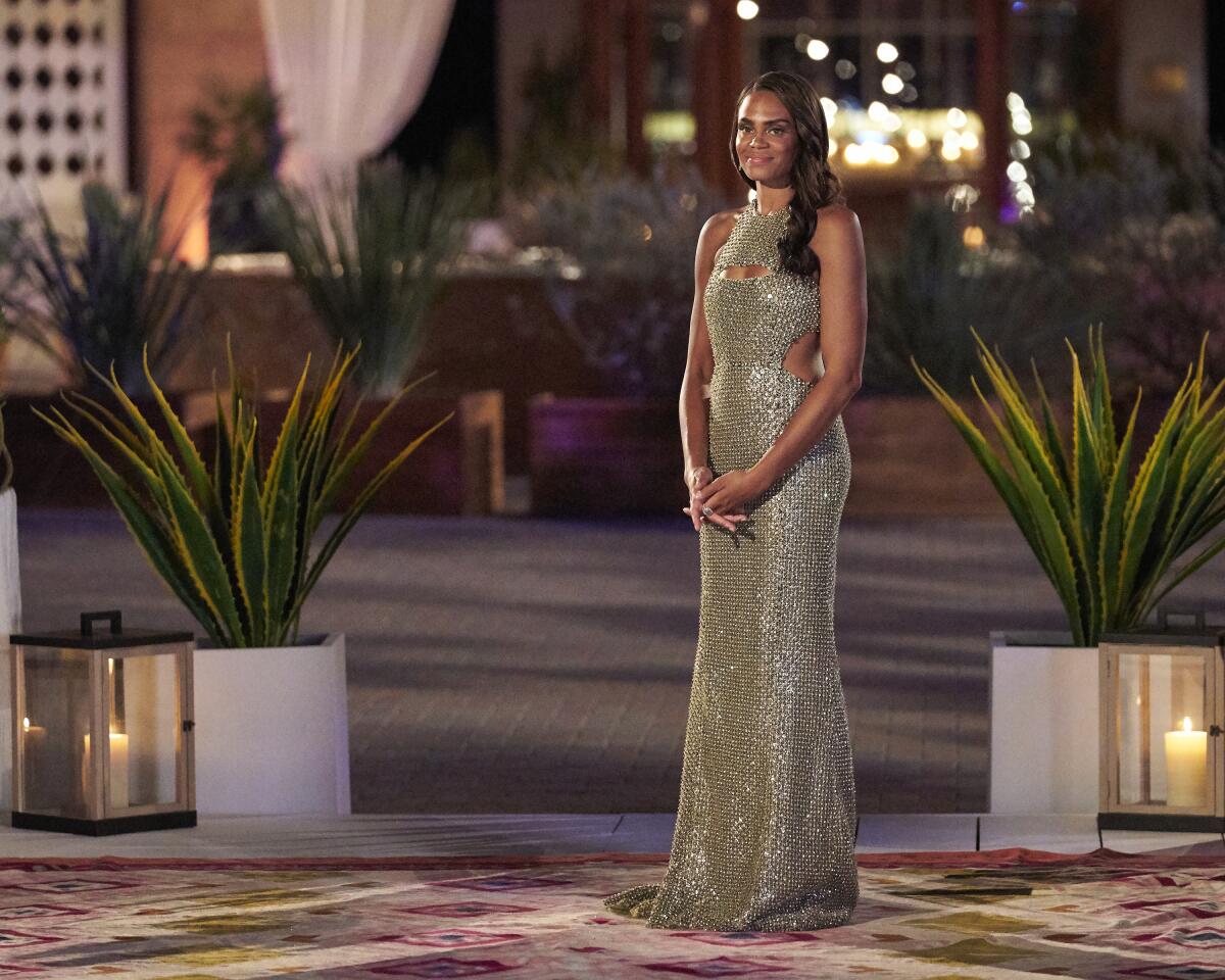 A woman in a floor-length sequined green gown standing between two plants