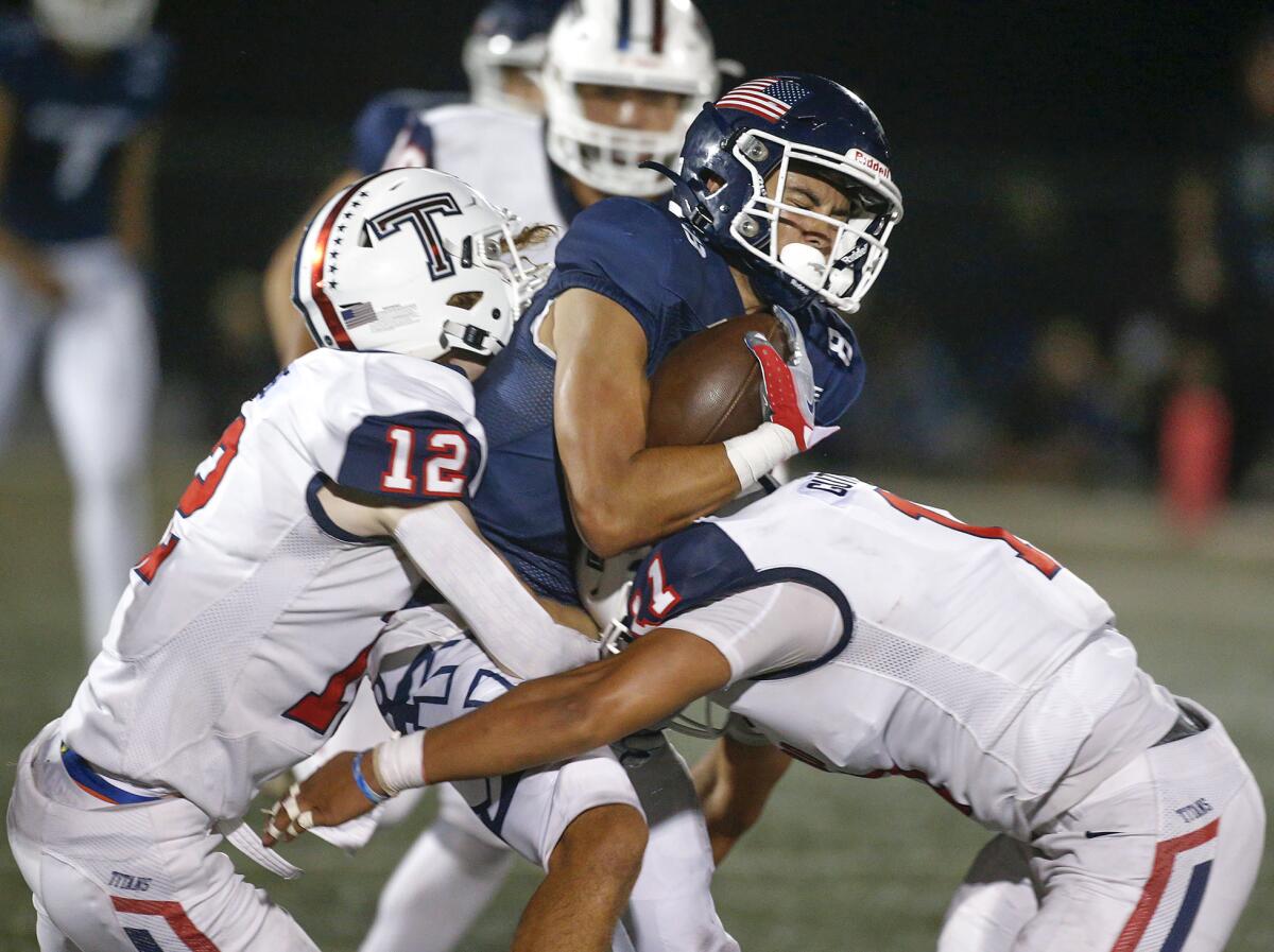 Newport Harbor's Josiah Lamarque (8) is tackled by two Tesoro defenders.