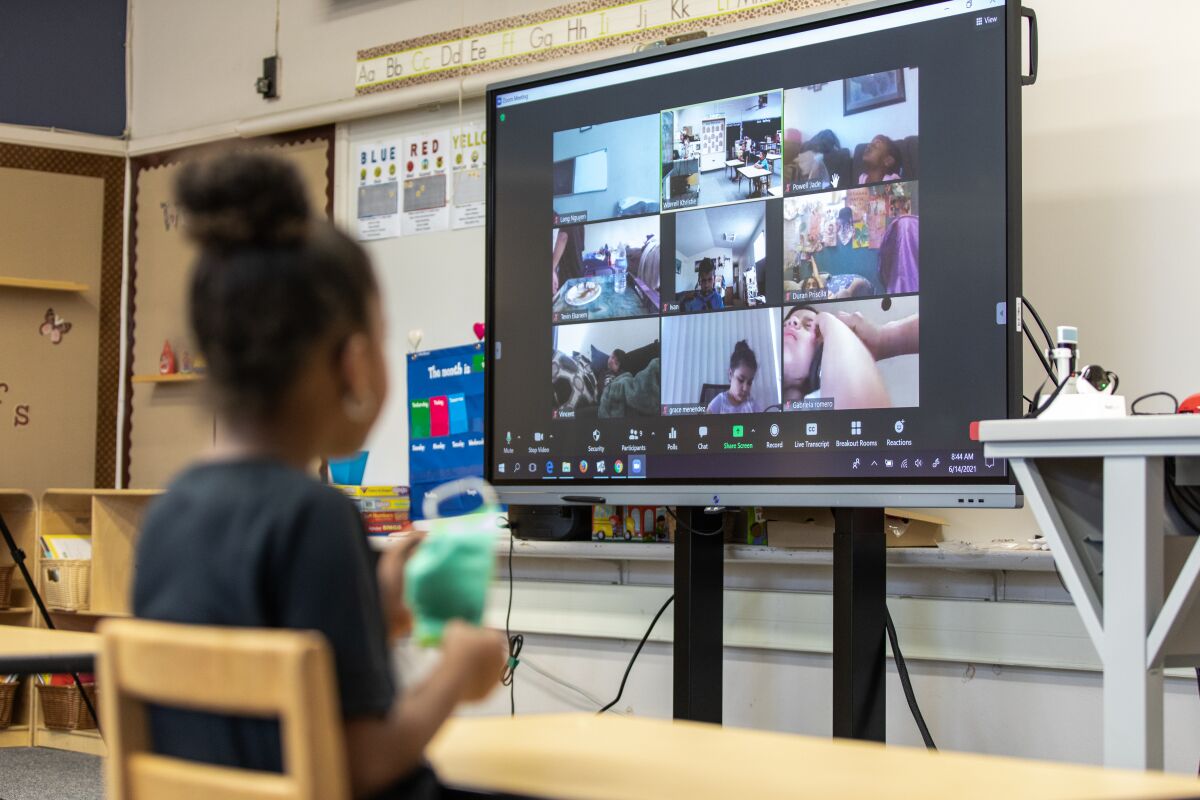 Students learn in Valencia Park Elementary classroom with a screen showing other students learning from home