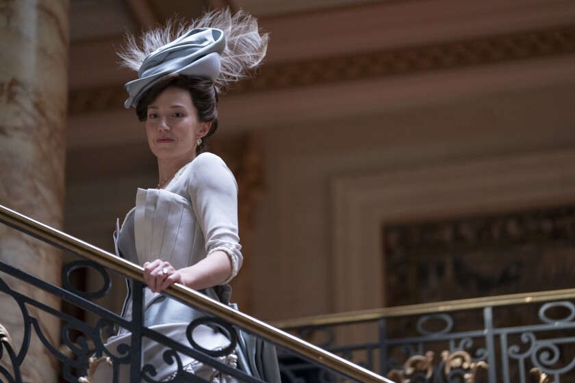 A woman in an elaborate light blue dress and hat ascends a staircase