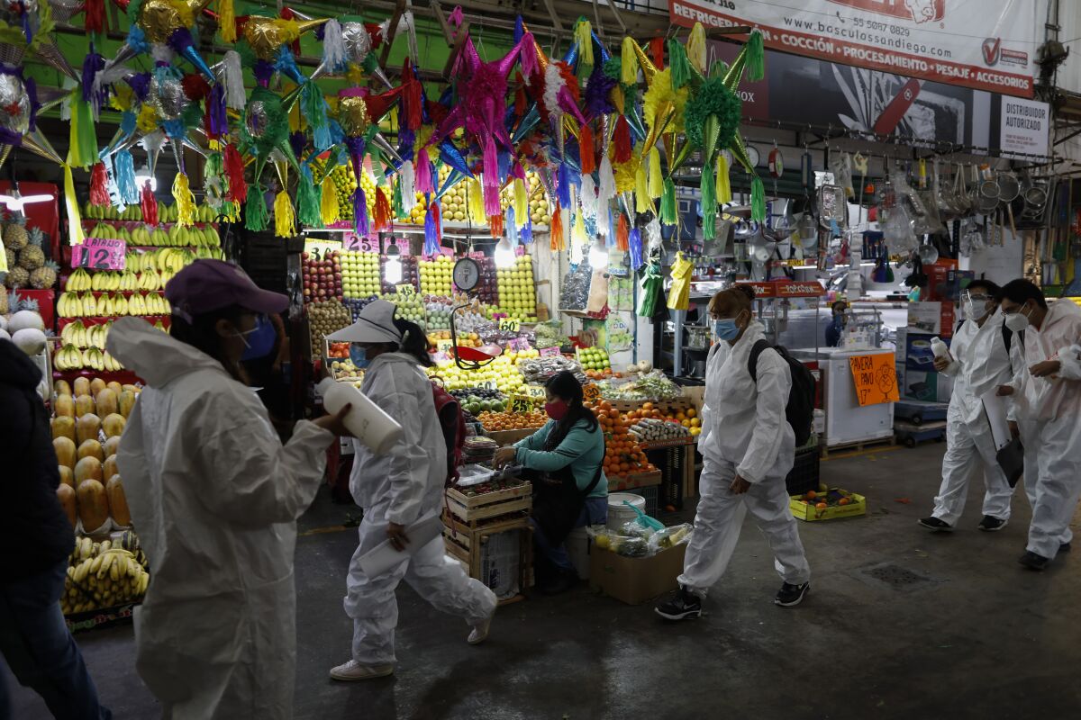 Workers wearing protective suits walk to take up positions to dispense antibacterial gel to passing shoppers and workers, inside the Central de Abastos, the capital's main market, in Mexico City, Tuesday, Dec. 8, 2020.(AP Photo/Rebecca Blackwell)