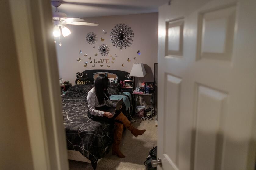 LAKE ELSINORE, CA - DECEMBER 14, 2022: Venezuelan asylum seeker Lisseth, 45, works on her computer in her bedroom on December 14, 2022 in Lake Elsinore, California. She was sponsored by a U.S. citizen to come to the United States. ***PLEASE DO NOT LIGHTEN PHOTO. THE WOMAN MUST REMAIN IN SHADOW AND CAN'T BE IDENTIFIED FOR HER SAFETY**(Gina Ferazzi / Los Angeles Times)