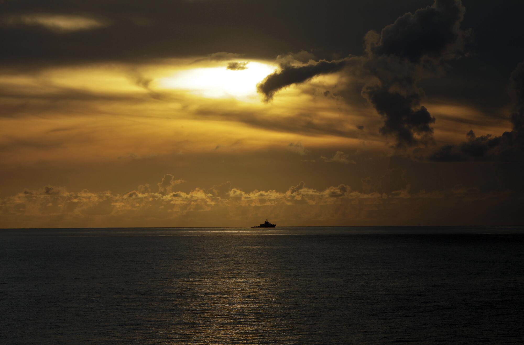 A ship far off on the horizon under a darkening yellow-orange sky