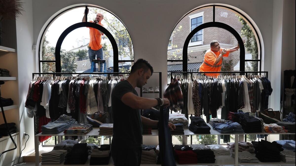 Jeff Doss, left, and Ivan Rodriguez, right, work on the exterior of the clothing store Towne by Elysse Walker, located at Palisades Village. Inside the store folding clothing is floor coordinator Jason Rosenwach.