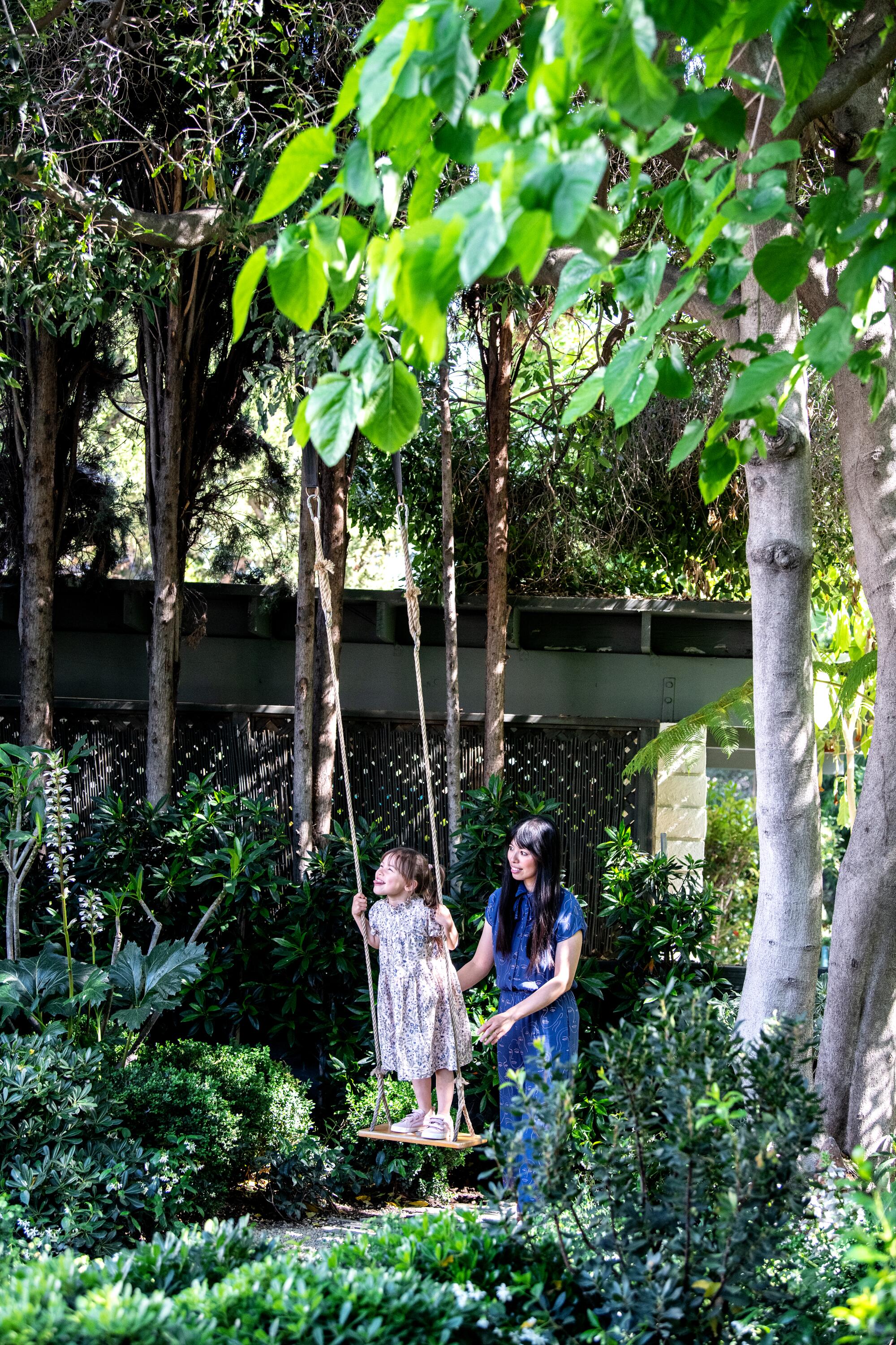 A woman pushes a child on a swing in a garden