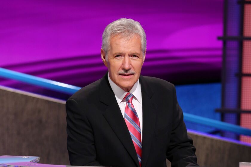 Alex Trebek leaning over the 'Jeopardy!' podium