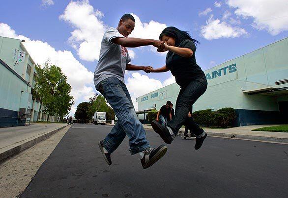 Mykel Polk, 16, and Areli Martinez, 18, practice a skateboard jump together during lunch on Saint Street, a road that cuts through the 25-acre campus. The schools disjointed layout has made it hard over the years to keep the campus free of vandalism. It also made it easier for students to ditch classes. Charter-school operator Green Dot clamped down this year with a heavy security presence and strict rules, which limited student opportunities for blowing off steam during breaks. But Green Dot has loosened up a bit, allowing skateboarding, pickup soccer games and other activities in selected areas.