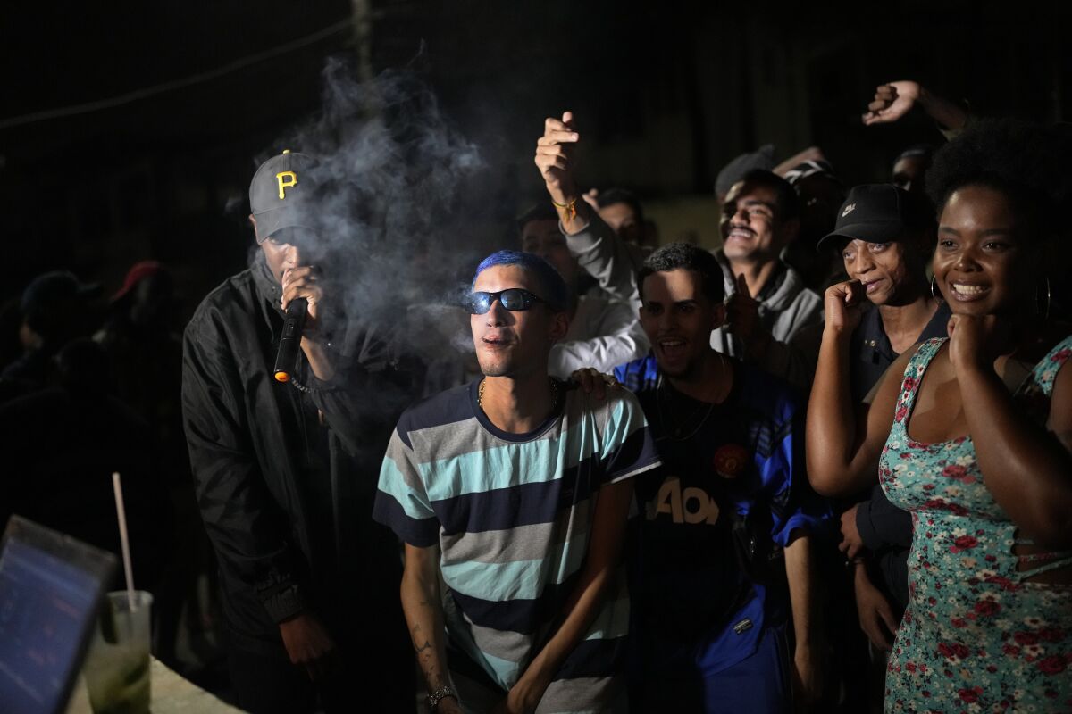 Rap artist Kunk, center, listens to a competitor at the Gas Battle rapping competition outside a bar in the City of God favela of Rio de Janeiro, Brazil, late Wednesday, Nov. 10, 2021. Rap artists in the favela are starting to compete again since the COVID-19 pandemic curtailed public gatherings, presenting local residents with a show in a sign of a return to normalcy for music lovers. (AP Photo/Silvia Izquierdo)