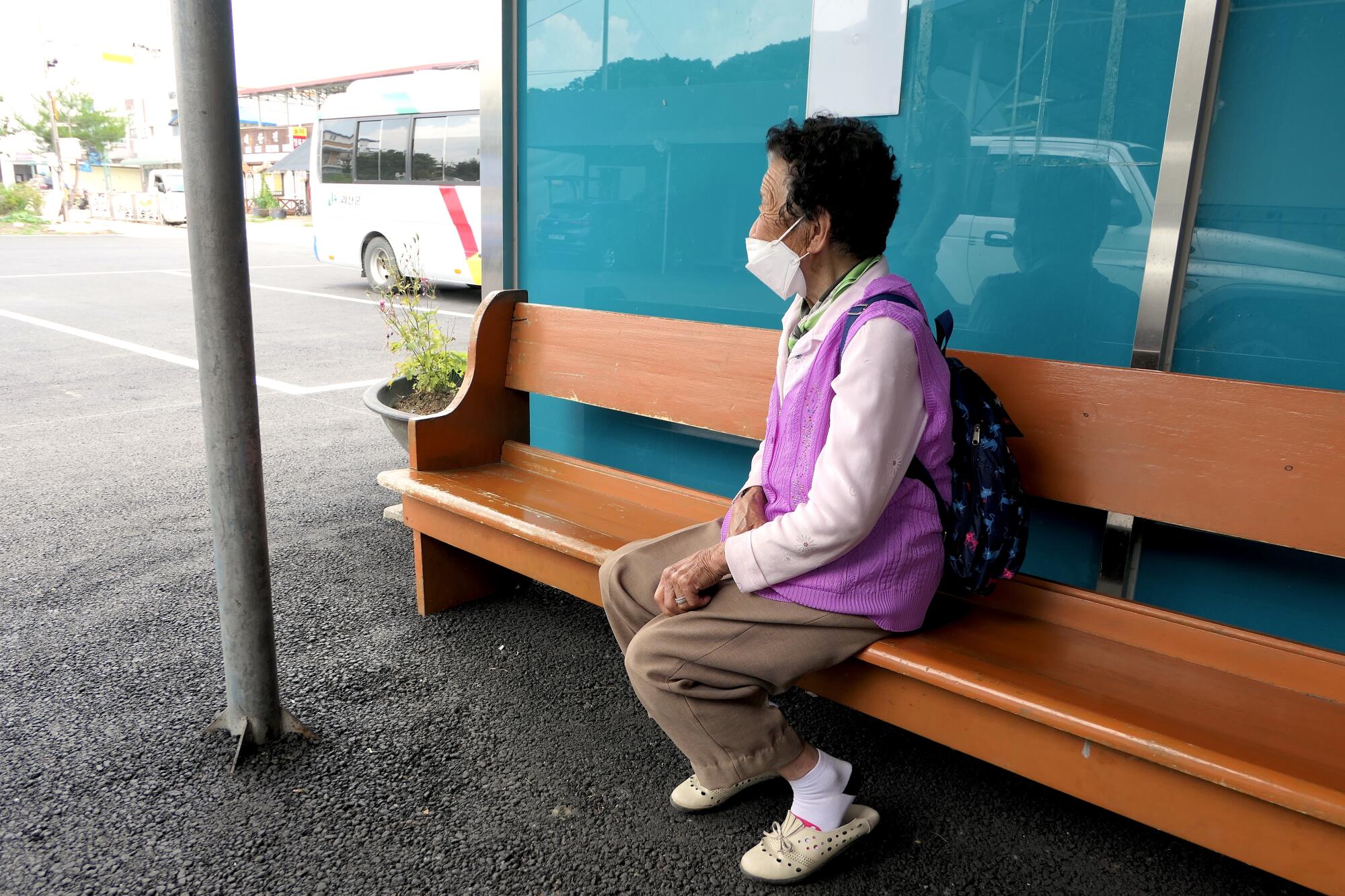 A woman wearing a knapsack sits on a bench  