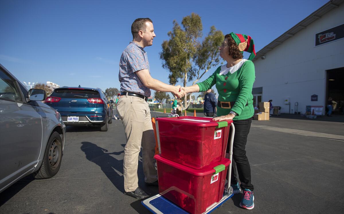 John Corwin receives a handshake from Marilyn Smith after dropping off gifts last year at the OC Fair & Event Center for two families for Share Our Selves' annual Adopt A Family program. The deadline for donors to participate this year is Dec. 11.