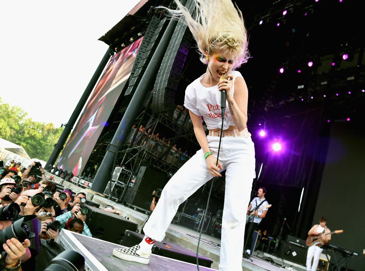 A woman swirls her platinum blond hair as she sings into a microphone on a stage.
