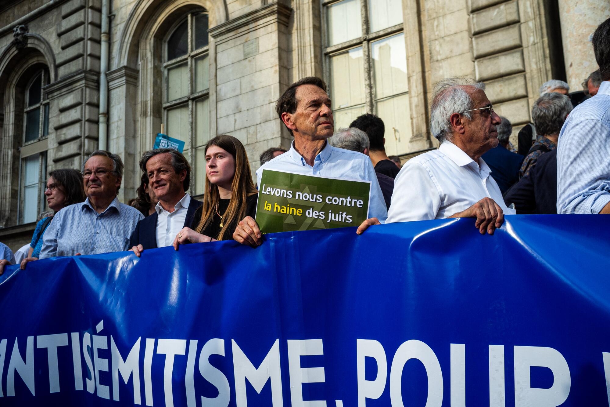 Protesters stand behind a banner, one holding a sign reading, "Let's rise against the hate of Jews," in Lyon, France.