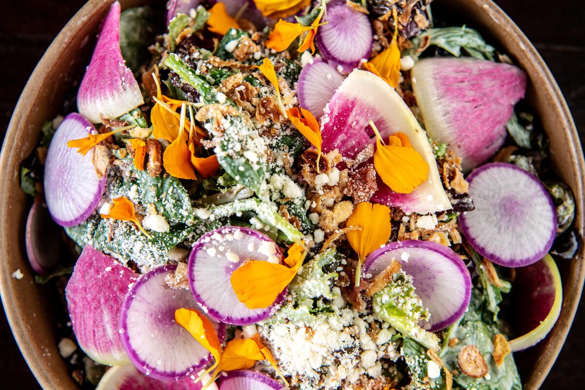 Closeup of a bowl filled with greens, sliced radishes and flower petals in a salad.