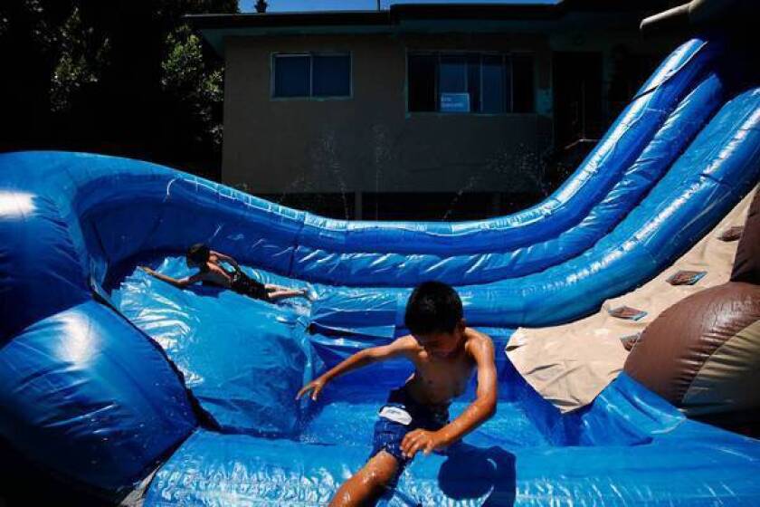 On a very hot day in L.A., David Murillio, 8, left, and Joshua Rodriguez, 9, cool off in a two-story inflatable pool in Boyle Heights. The boys were on their way to Pecan Recreation Center when they saw their neighbor's rented pool and jumped in. The last significant heat wave to hit Southern California was five years ago, a National Weather Service specialist said.