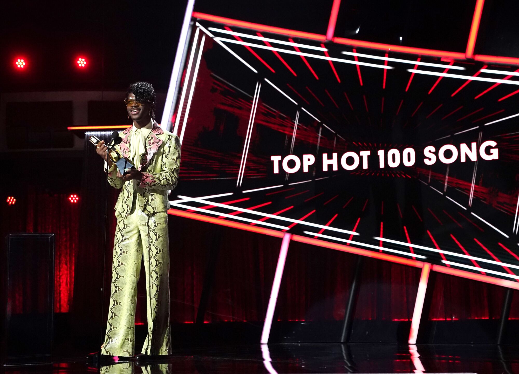 Lil Nas X, in gold patterned pants and jacket, holds his award. 
