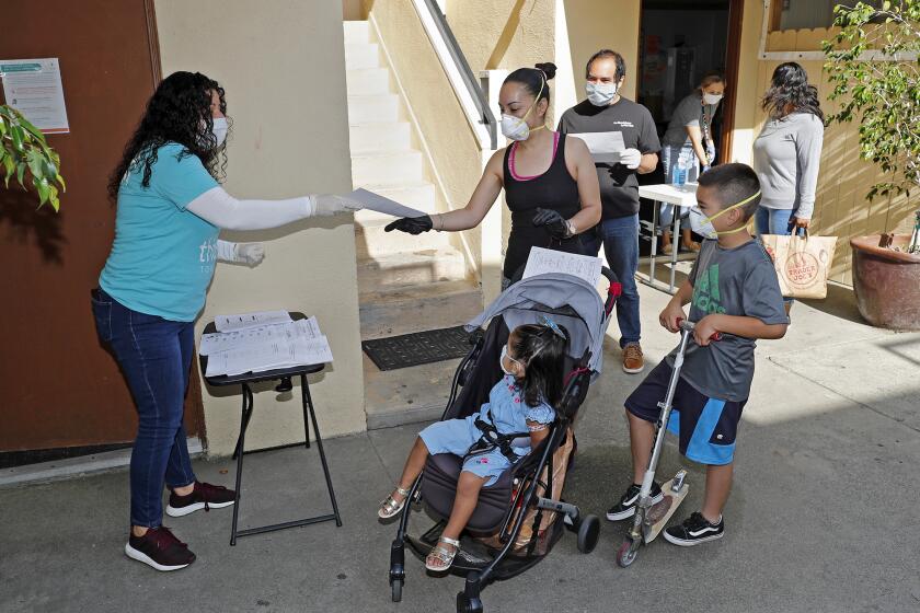 Ruth Malagon, left, family and community coordinator for the elementary program, hands a learning packet to Sindia Chavez, center, with her daughter Andrea, 2, and son Marco, 8, at Shalimar Learning Center in Costa Mesa on Tuesday morning. Shalimar Learning Center in Costa Mesa has pivoted its usual after-school programs to help its neighborhood community. The center is giving out $100 debit cards, as well as providing food and school supplies to community members.