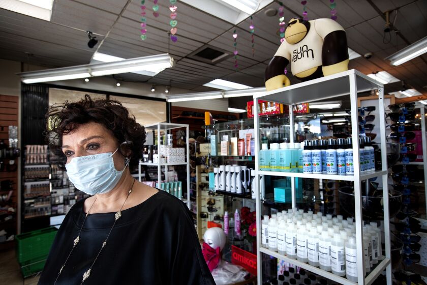 SHERMAN OAKS, CA-MAY 15, 2020: Janet Tavakoli, 69, owner of Sherman Oaks Beauty Collection, wearing a protective mask against the coronavirus, is photographed next to bottles of hand sanitizer, right, for sale inside her store. The store is one of 60 non-essential businesses cited by Los Angeles City Attorney Mike Feuer for "flouting the city's Safer at Home order. Tavakoli says she shut down her store for 2 weeks, losing $15,000 in sales but reopened after seeing beauty store competitors open. (Mel Melcon/Los Angeles Times)