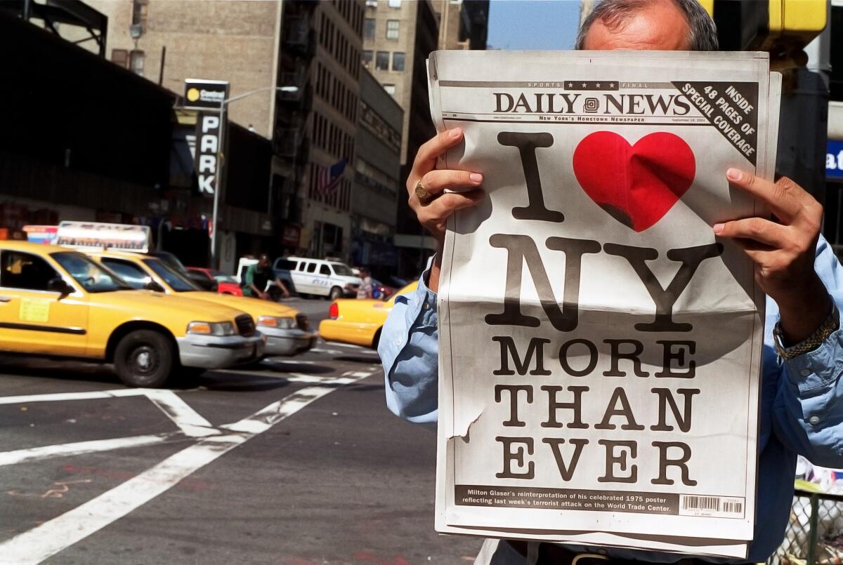A man holds up a copy of the New York Daily News with a logo reading "I Heart New York"