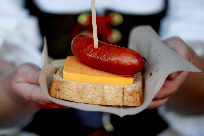 A fat sausage and slab of cheese sit on a thick slice of bread.