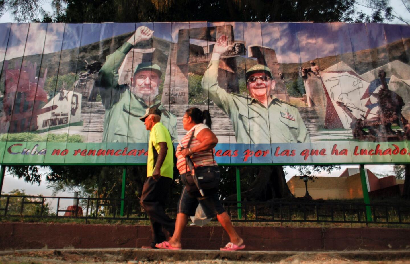 A couple walks next to a poster of Cuban President Raul Castro and former Cuban president Fidel Castro in Guantanamo, Cuba, on March 13, 2016.