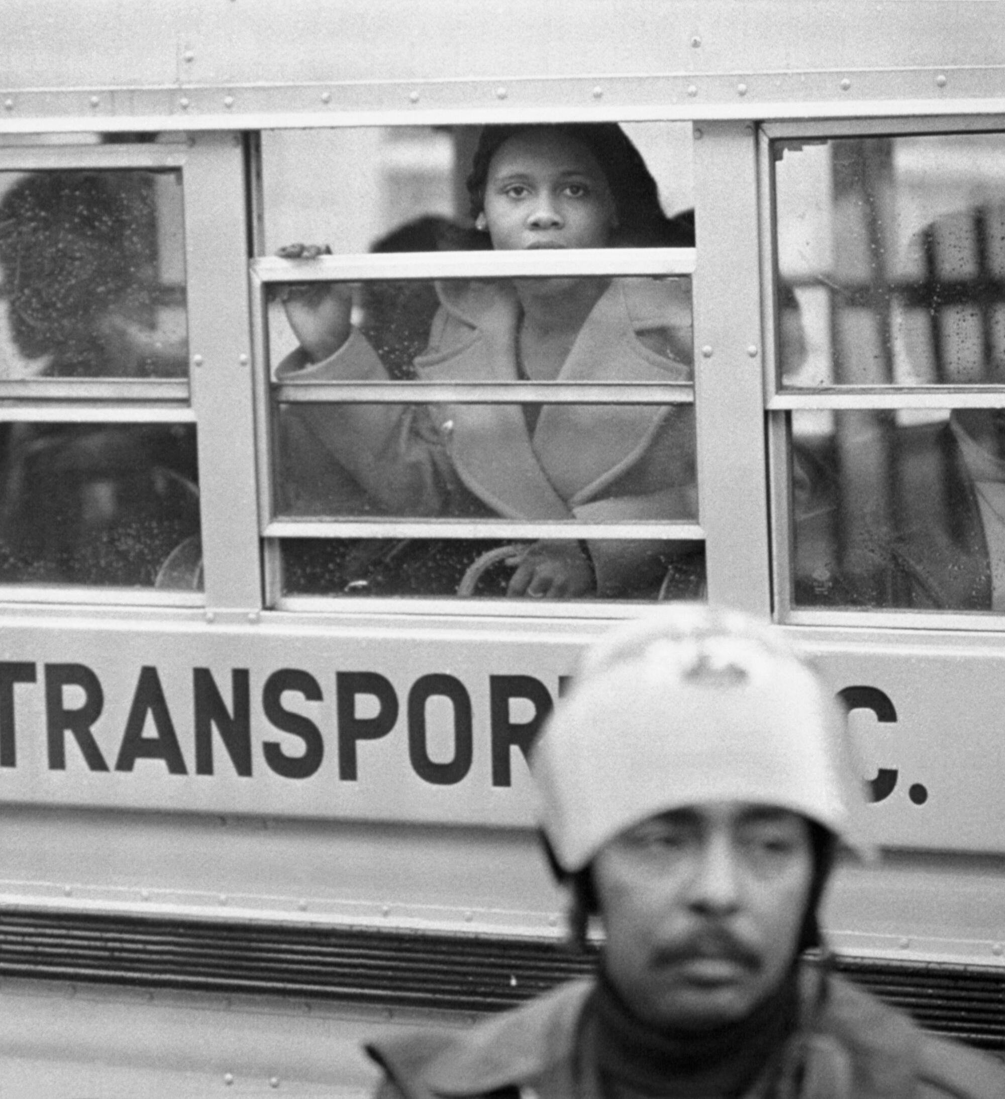 A student looks out the window of a school bus while a police officer stands in front of it.
