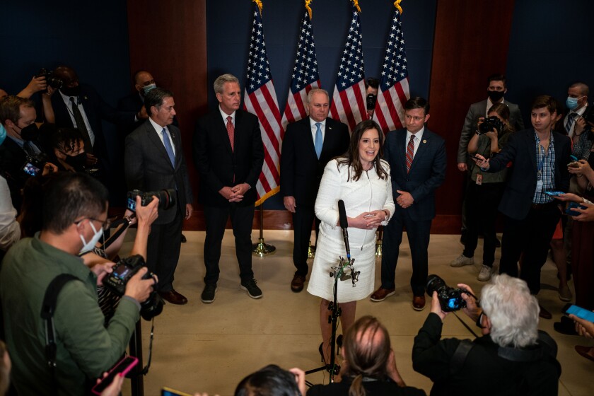 Rep. Elise Stefanik speaks to journalists with a row of men in suits behind her.