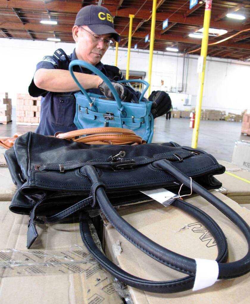 Customs officer Jesus Uyquiengco examines some of the 1,500 counterfeit Hermes handbags that were seized at the Port of Los Angeles.