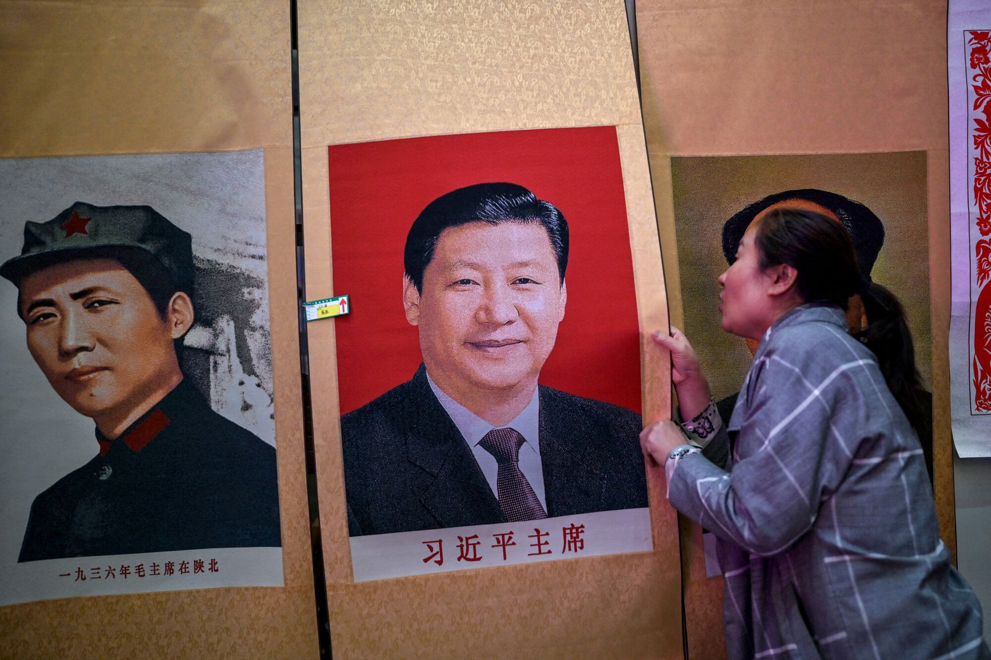 A woman holds a color poster depicting a smiling man next to another poster of a Chinese revolutionary 