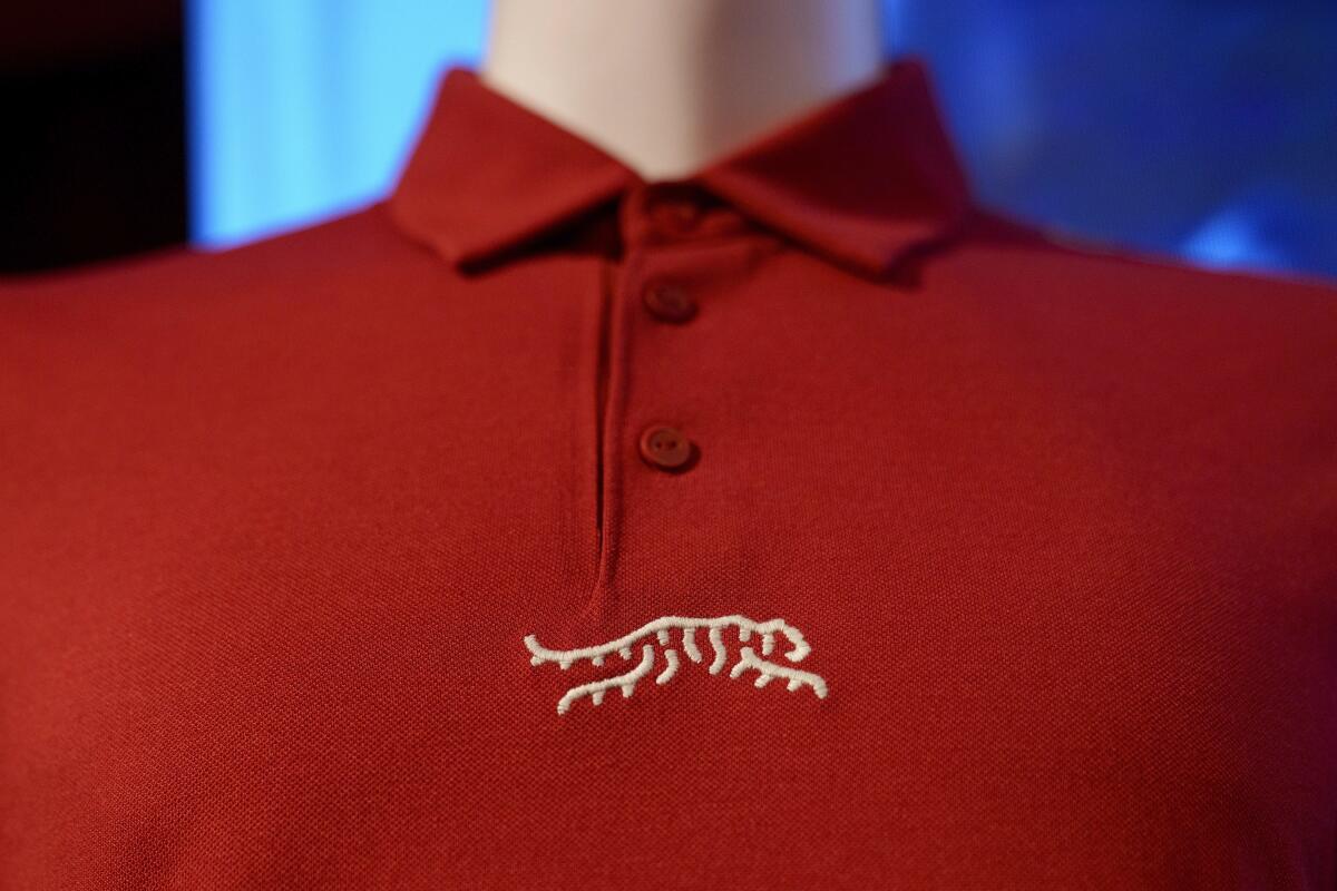 A red polo shirt with a tiger logo under the buttons is displayed from Tiger Woods' new clothing line.