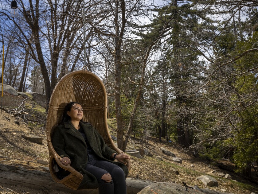 A woman sits in a swing chair in the mountain trees.