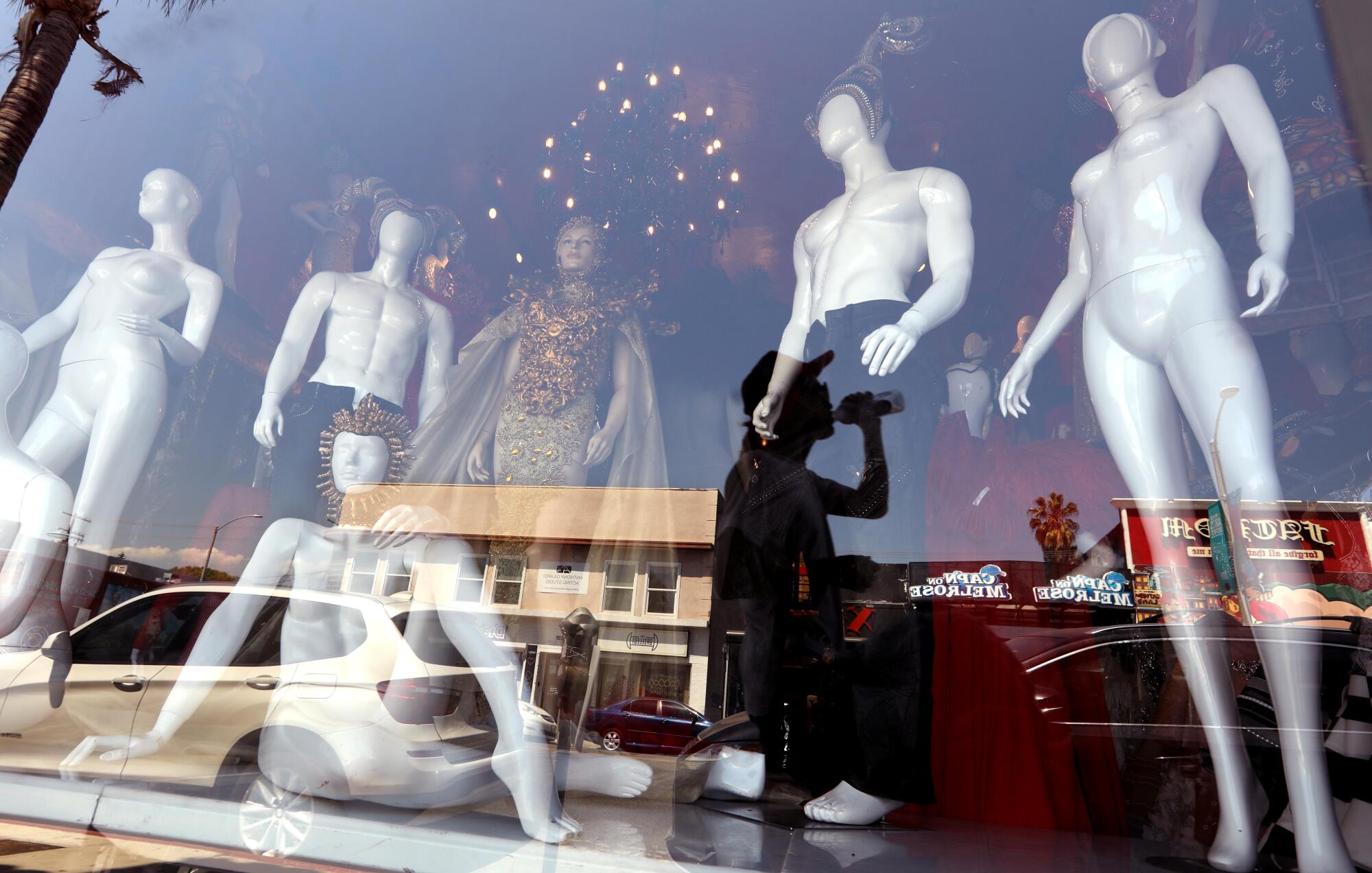 The image of a pedestrian drinking is reflected in a shop window displaying mannequins