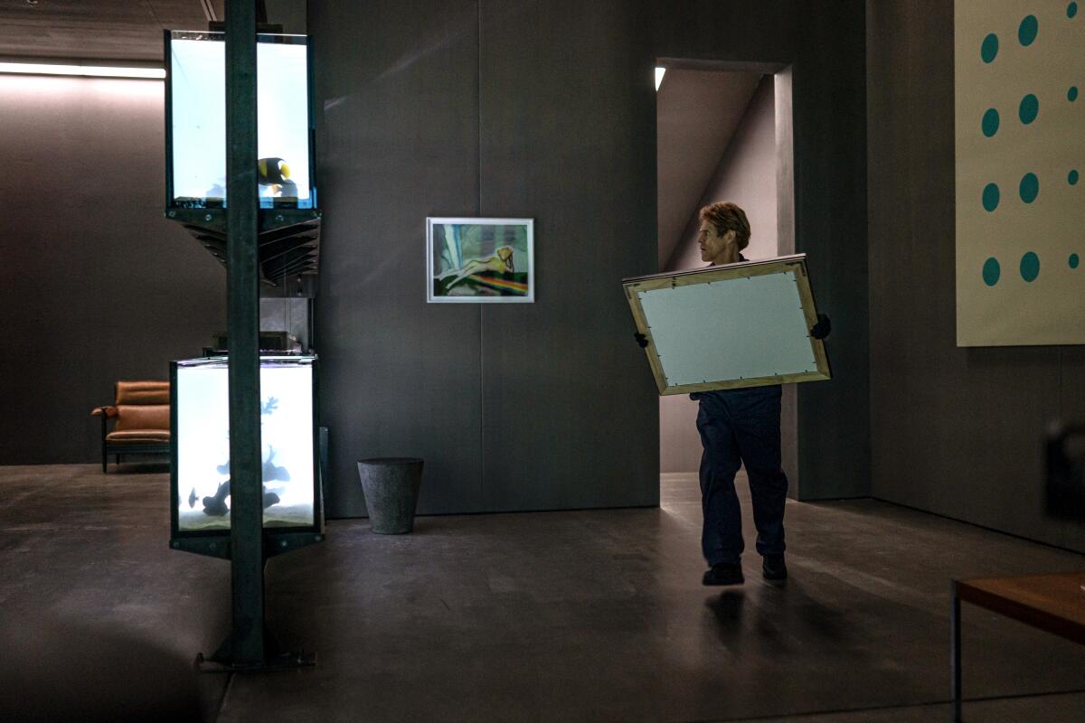 A man holding a framed artwork stands in a darkened room.