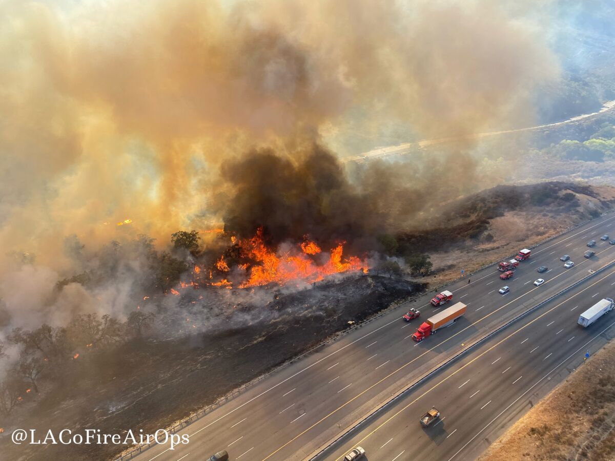 An aerial photo shows a wildfire off Interstate 5 as traffic drives past.