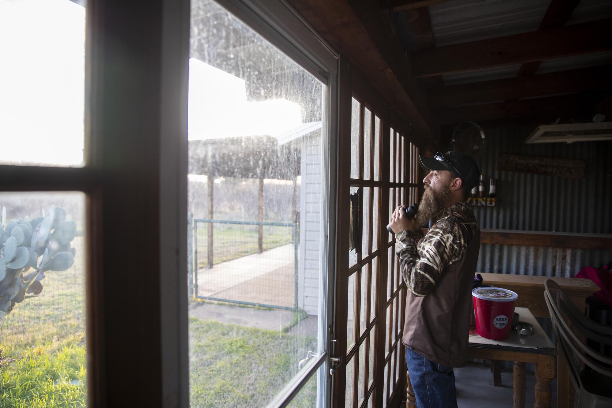 Fred Jones keeps an eye out for wild hogs in a wheat field from inside a rural cabin bunkhouse in Throckmorton County, Texas.