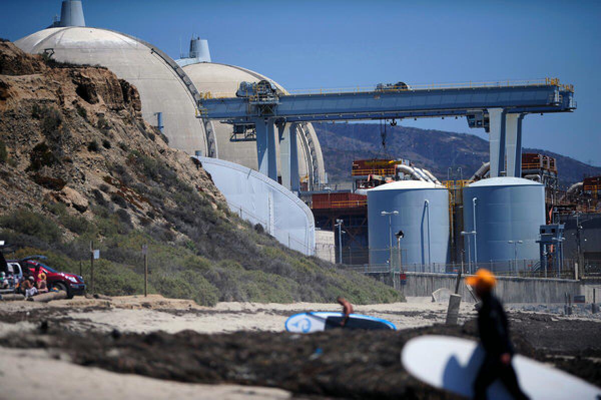 Surfers walk along a beach nearby the San Onofre nuclear power plant in 2012. Southern California Edison announced Friday that it would close the facility.