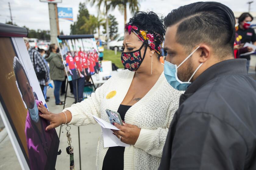 Irene and Matthew Rodriguez look at a photograph of their father Armando Rodriguez, who died of covid, during a rally demanding stronger COVID-19 protections for caregivers and patients at Fountain Valley Regional Hospital on Monday, November 23.