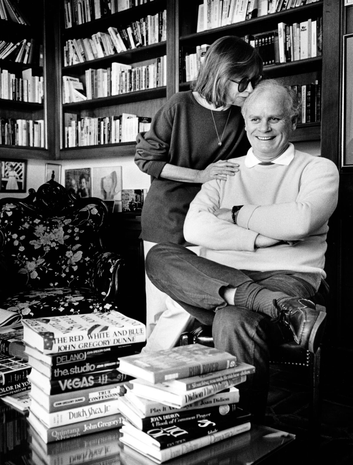 Black and white photo of a woman kissing a seated man on the head surrounded by books