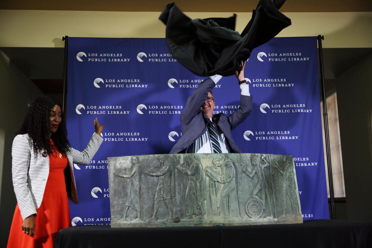 The director of the Los Angeles Central Library, Kren Malone, left, watches as City Librarian John F. Szabo unveils the recovered piece of the long-lost Well of the Scribes sculpture.