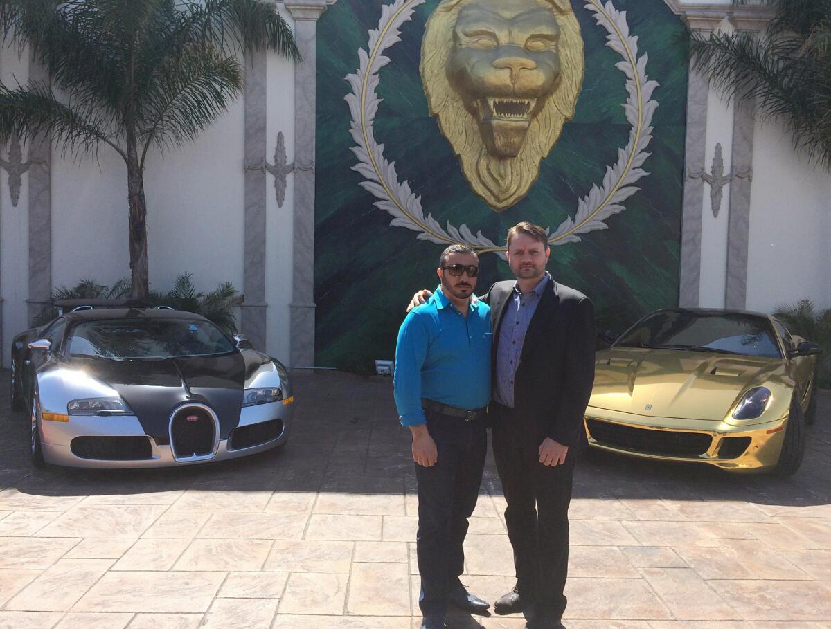 Two men pose in front of luxury cars