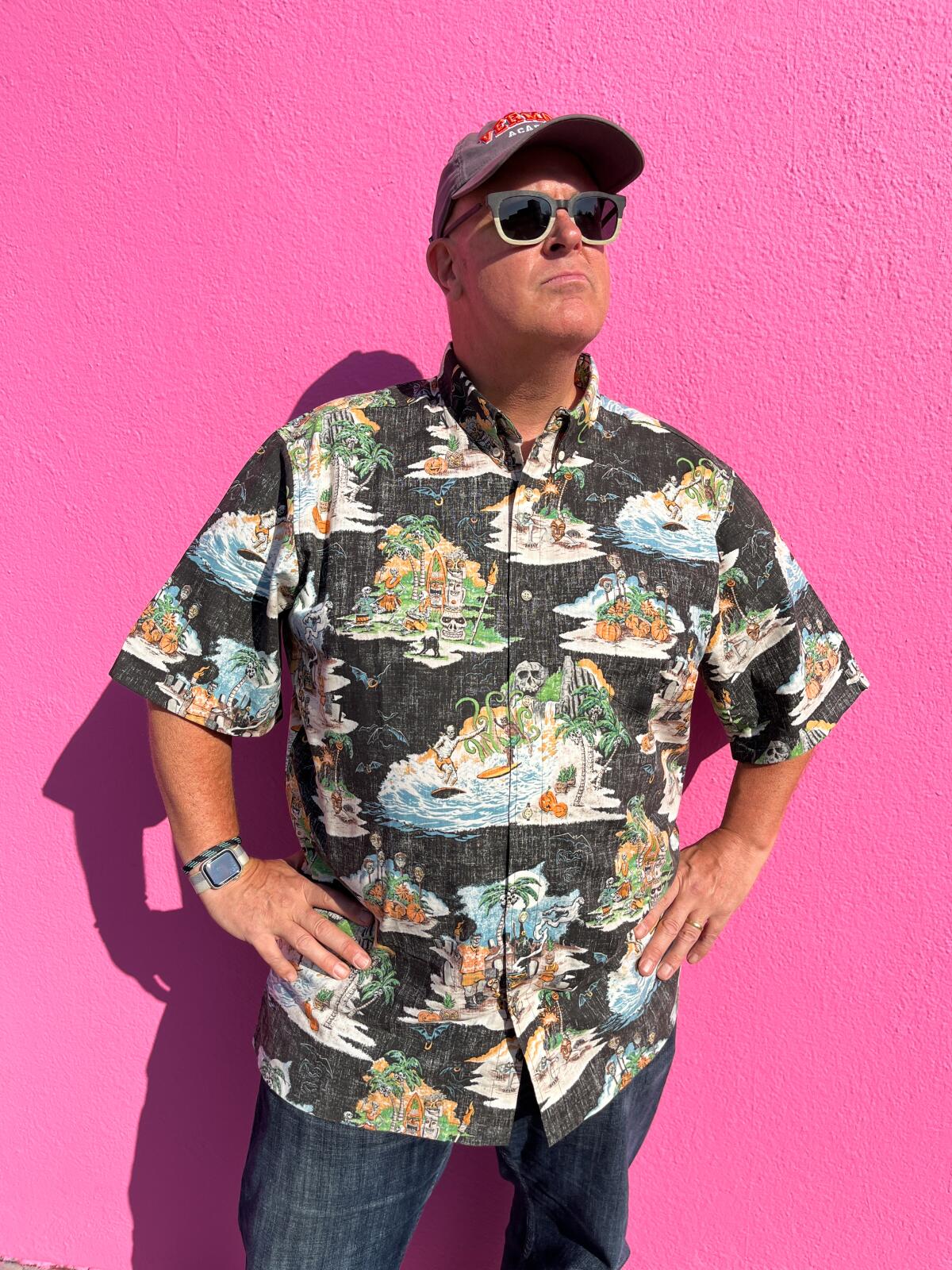 A man stands with his hands on his hips in front of a bright pink wall