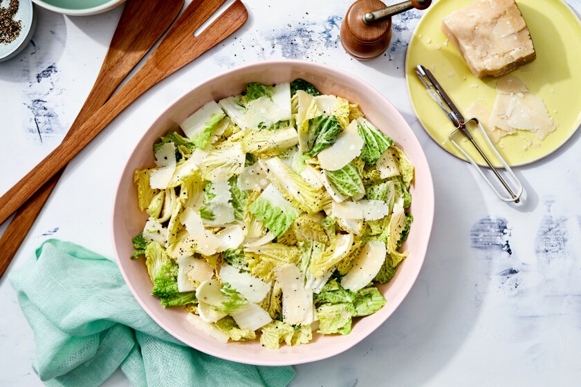 A bowl of Nappa Cabbage Caesar Salad with wooden serving utensils.