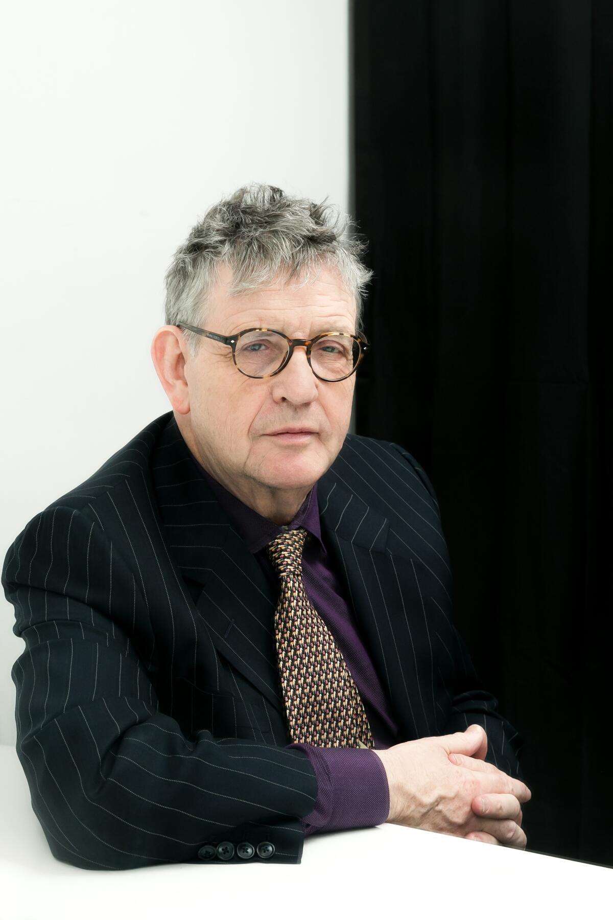 A gray-haired man with glasses in a dark shirt and jacket.