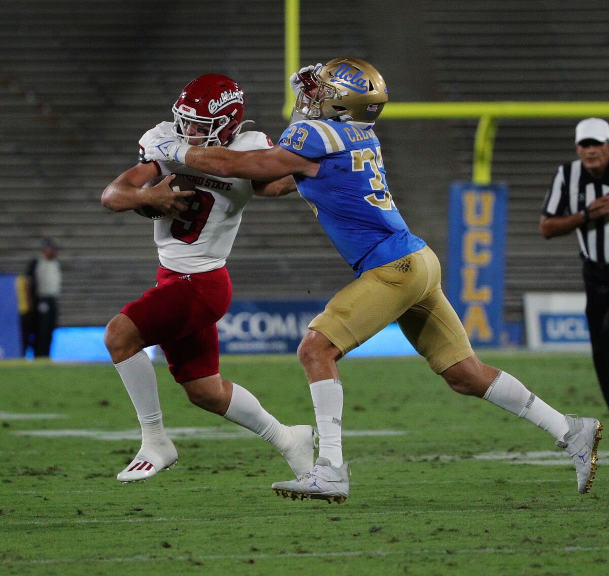 Fresno State quarterback Jake Haener extends his arm to UCLA linebacker Bo Calvert as he scampers for extra yardage.