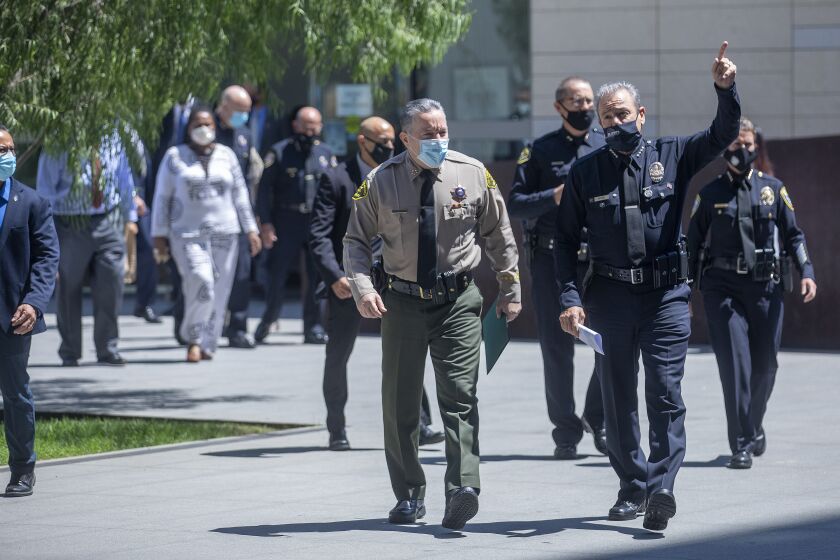 LOS ANGELES, CA - AUGUST 26, 2020: Los Angeles County Sheriff Alex Villanueva, front, center, and LAPD Chief Michel Moore, right, arrive with other officials for start of a press conference held outside of LAPD Headquarters in downtown Los Angeles, announcing significant crime arrests made by the multi-agency SAFELA Task Force, which was formed to investigate crimes that occurred during protests and demonstrations in Los Angeles back in May and June. The LAPD has arrested 14 people as a result. (Mel Melcon / Los Angeles Times)