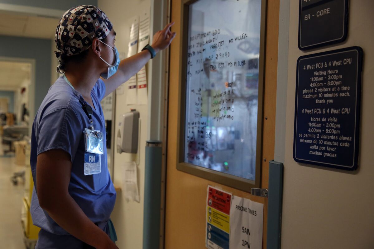 A nurse checks notes written on a windowpane on a patient's door