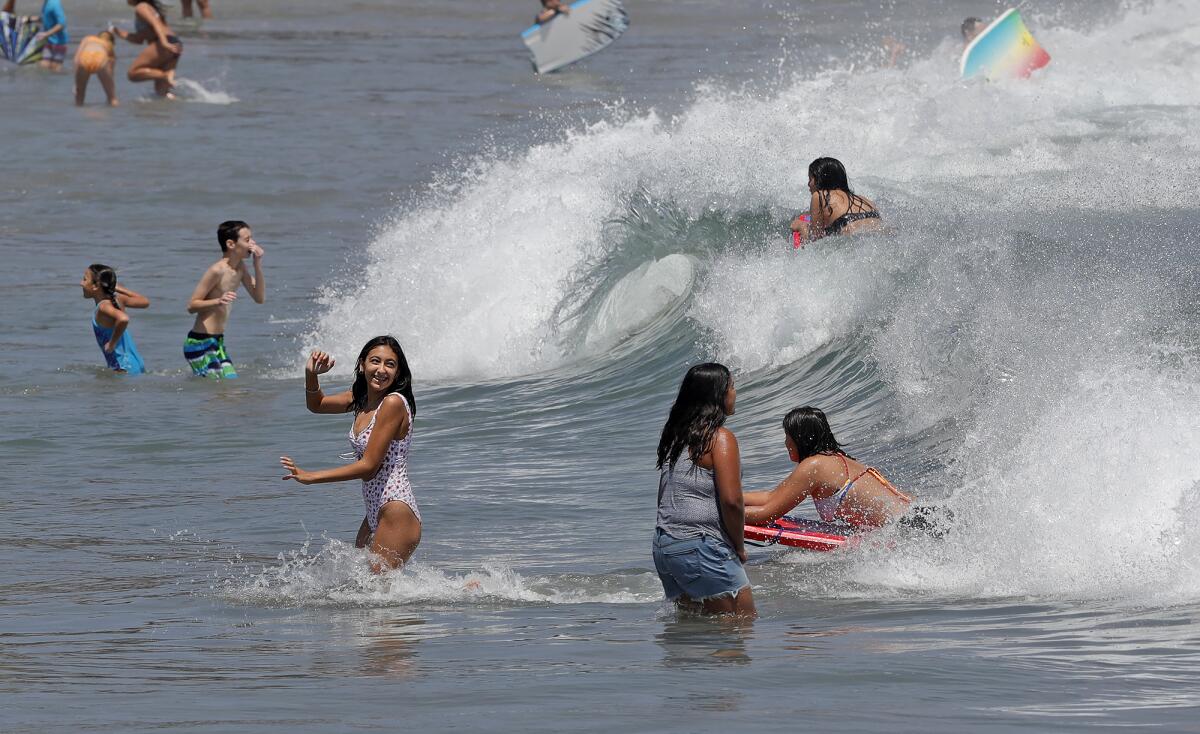 Children jump into the waves at Corona del Mar State Beach in Newport Beach on Tuesday.