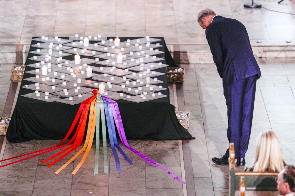 Prime Minister Jonas Gahr Store bows near candles and a rainbow-colored set of ribbons on a table.